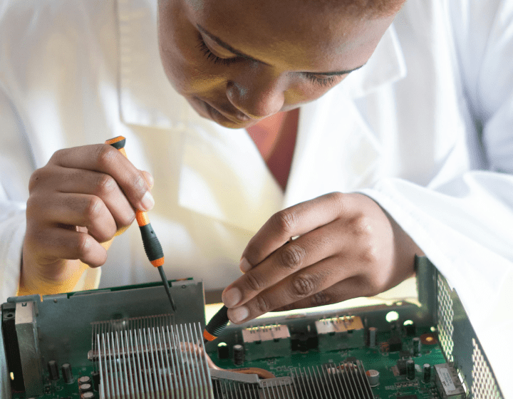 Person in a white lab coat working on an electronic circuit board with a screwdriver.