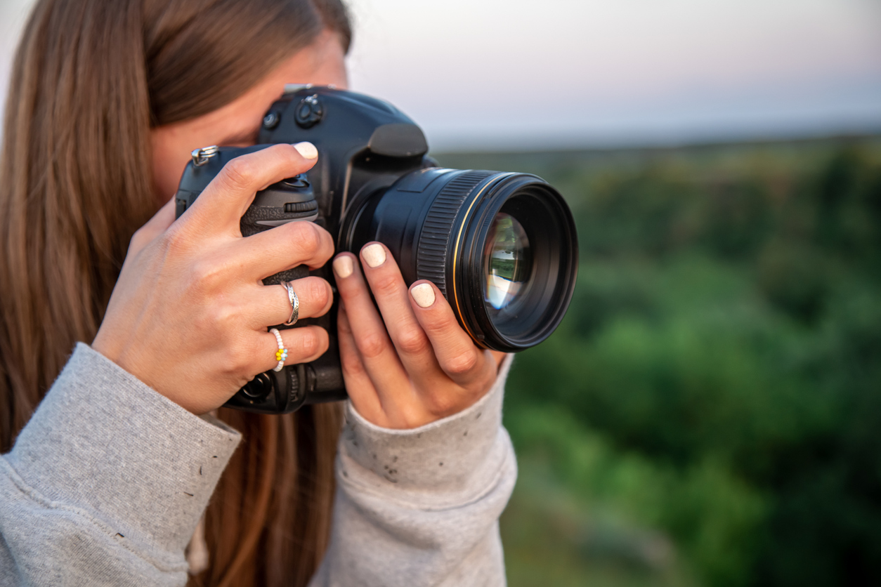 A young woman with a professional camera takes a photo in nature.