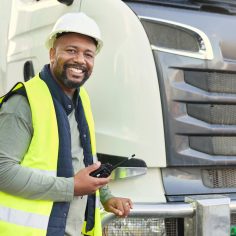 Construction worker in shipping business by delivery truck in shipyard. Black man truck driver with walkie talkie doing logistics, transport and export of cargo container in distribution industry