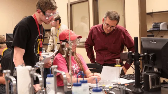 Three people in a lab setting working at a computer with lab equipment nearby.