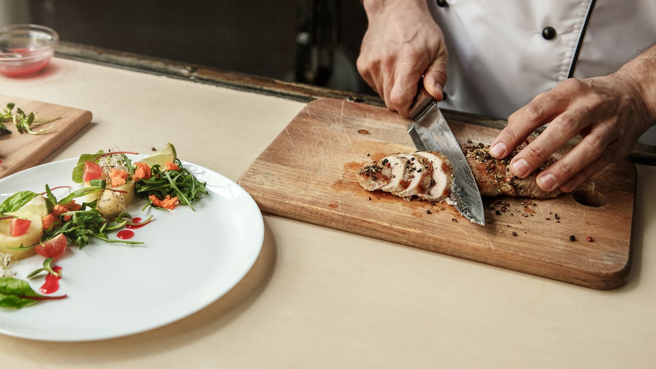 A man's hands chopping chicken on a cutting board.