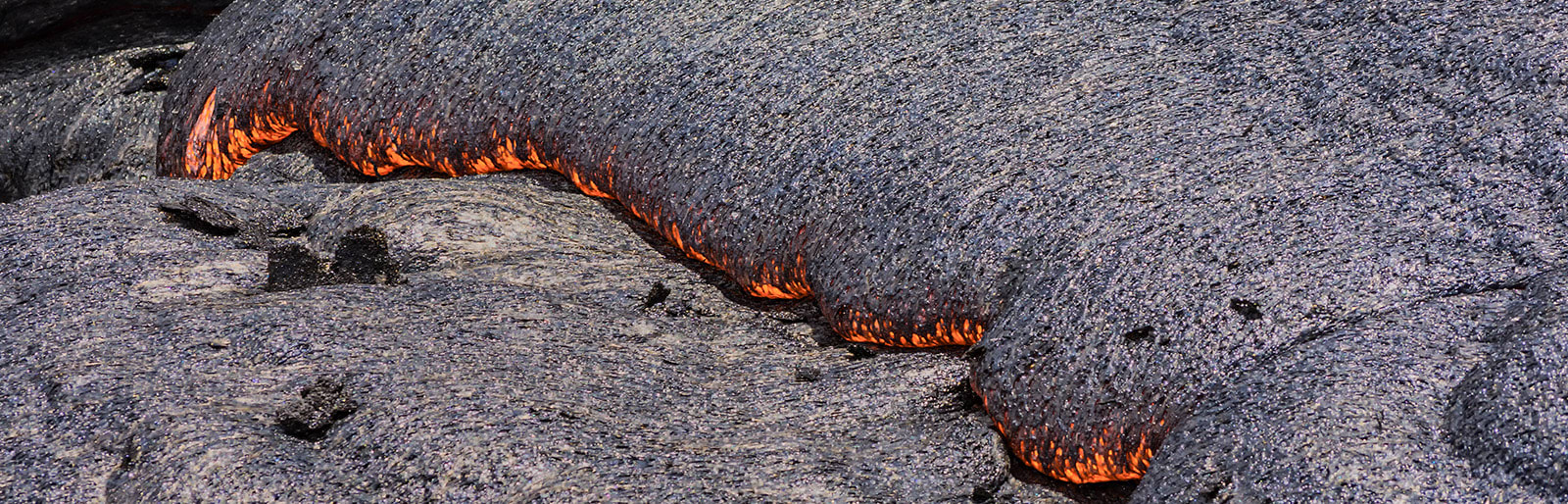 Flowing lava with bright orange edges on a dark, solidified lava surface.