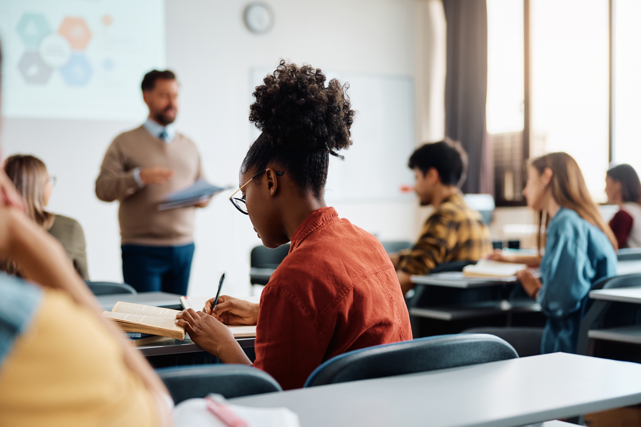 Black female student taking notes during a class in lecture hall.