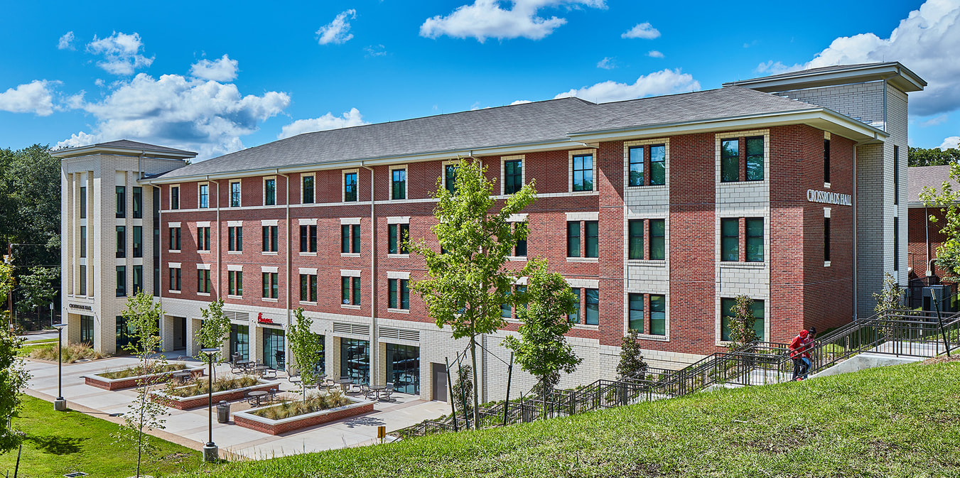 A four-story brick and stone building labeled Crossroads Hall, with a landscaped area and seating in front.