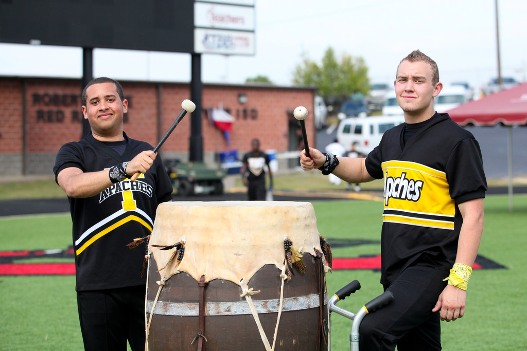 Two TJC students in Apache spirit uniforms stand beside a large ceremonial drum on the football field.