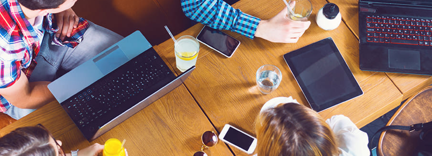 A group of people seated at a table, using laptops and enjoying drinks in a casual setting.