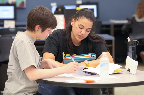 Two students sitting at a round table working together with notebooks and a water bottle in a tutoring or study session.